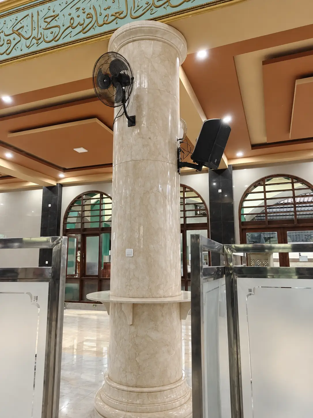 Tiang onyx marmer krem dengan meja lingkar di serambi masjid